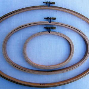 May include: Three wooden embroidery hoops of different sizes, nested together. The largest hoop is 8 inches by 12 inches.