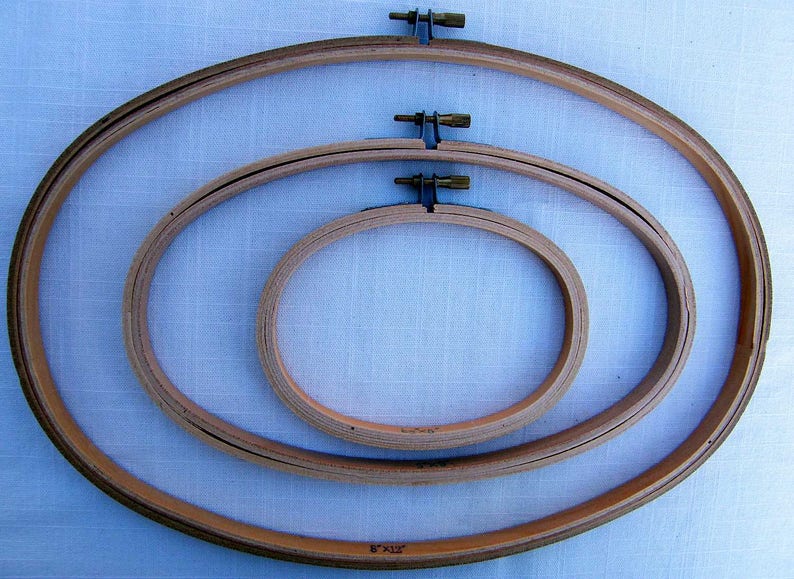 May include: Three wooden embroidery hoops of different sizes, nested together. The largest hoop is 8 inches by 12 inches.