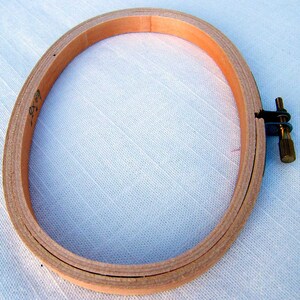 May include: A wooden embroidery hoop with a screw-on tightening mechanism. The hoop is 7 inches in diameter and is made of natural wood.