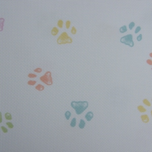Puede incluir: Tela blanca con un patrón repetido de huellas de patas de color pastel. Las huellas de patas son en tonos de rosa, amarillo, verde y azul.