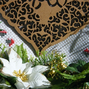 Pode incluir: Uma flor de poinsettia branca com detalhes dourados, cercada por folhagem verde e um ornamento em forma de cora&ccedil;&atilde;o de madeira marrom esculpido.