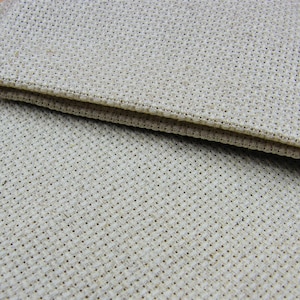May include: Close-up of two pieces of beige cross-stitch fabric. The fabric has a woven texture with small, evenly spaced holes, ideal for needlework. The edges are neatly finished, suggesting a craft project.
