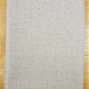 May include: Folded piece of beige cross-stitch fabric, suitable for embroidery projects. The fabric features a grid-like pattern of evenly spaced holes, ideal for detailed designs. The fabric is made of a natural fibre and is neatly folded.