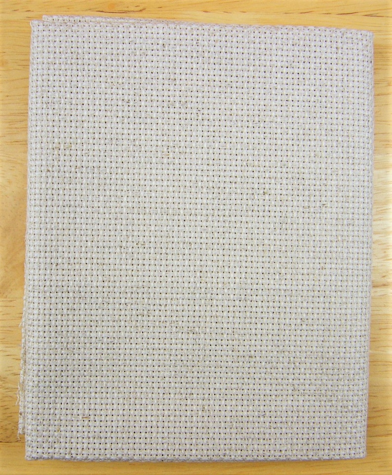 May include: Folded piece of beige cross-stitch fabric, suitable for embroidery projects. The fabric features a grid-like pattern of evenly spaced holes, ideal for detailed designs. The fabric is made of a natural fibre and is neatly folded.