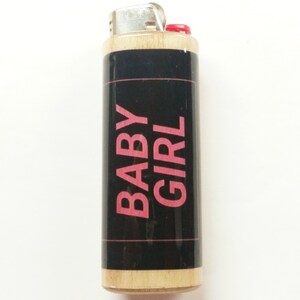 May include: A wooden lighter with a black label and pink text that reads "BABY GIRL".