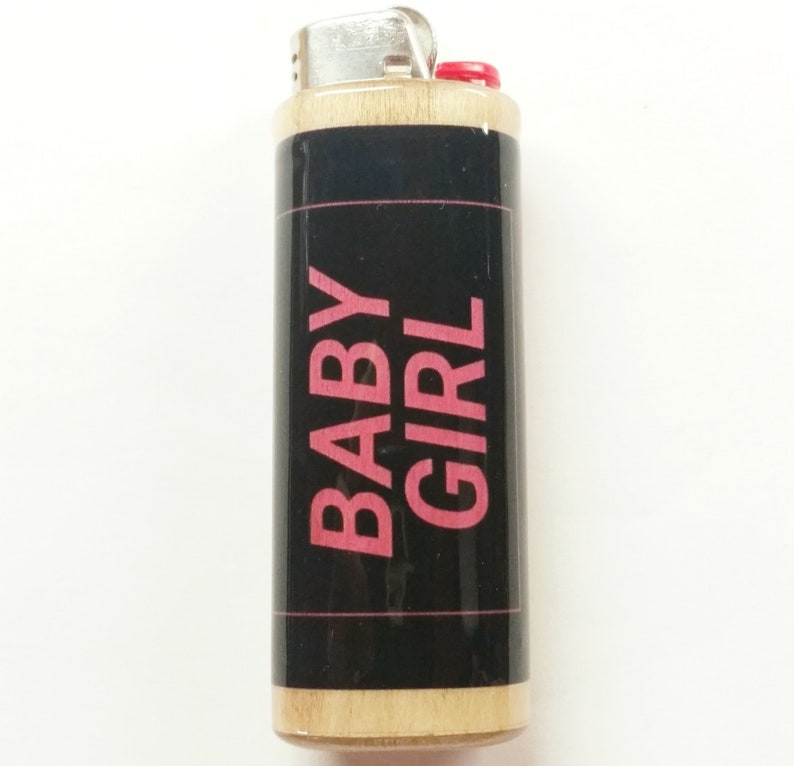 May include: A wooden lighter with a black label and pink text that reads "BABY GIRL".