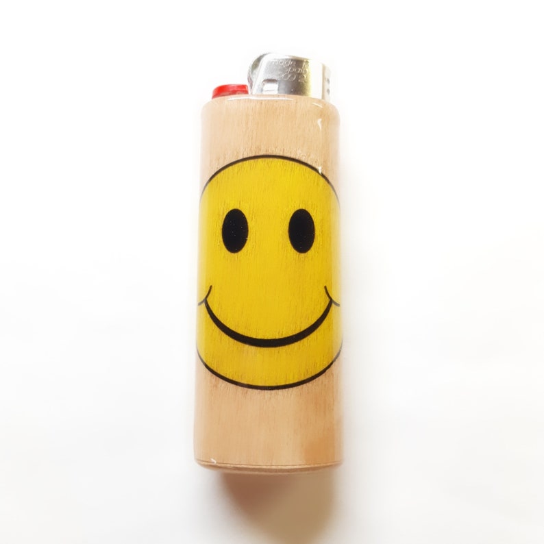 May include: A wooden lighter with a yellow smiley face design. The lighter has a red top and a silver metal hinge.