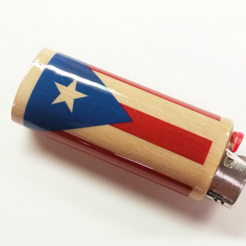 Peut inclure: Un briquet en bois avec un motif de drapeau portoricain rouge, blanc et bleu. Le briquet a un dessus en m&eacute;tal argent&eacute; et un bouton en plastique rouge.