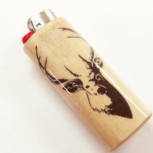 May include: A wooden lighter with a black and white deer head design. The lighter is made of natural wood and has a red plastic top.