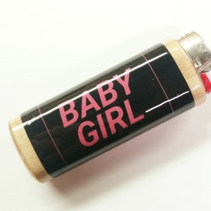 May include: A black and wood lighter with a pink "BABY GIRL" graphic.