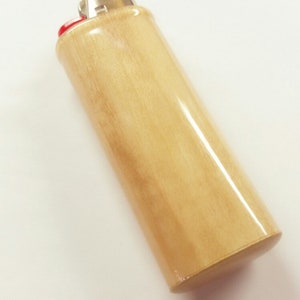 May include: A wooden lighter with a light brown finish. The lighter has a silver top and a red bottom.