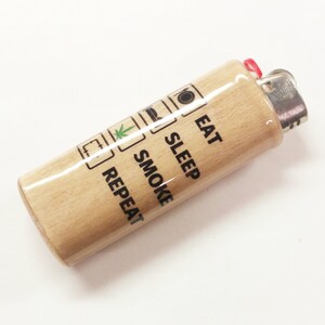 May include: A wooden lighter with a white and black design that says "Eat, Sleep, Smoke, Repeat".