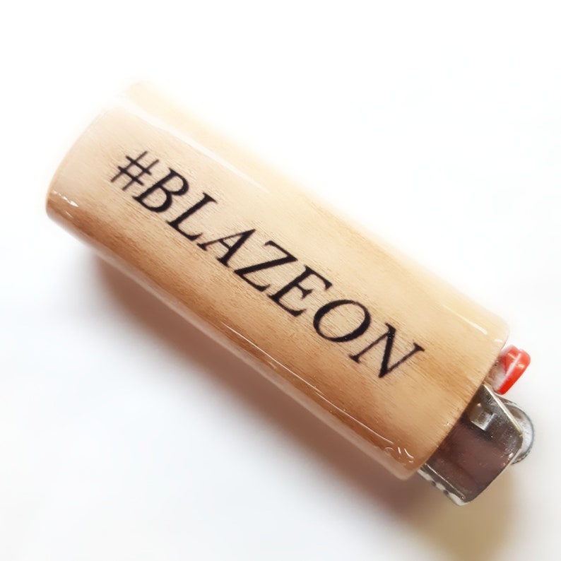 以下が含まれることがあります： 黒い文字で「#BLAZEON」と書かれた木製のライターです。