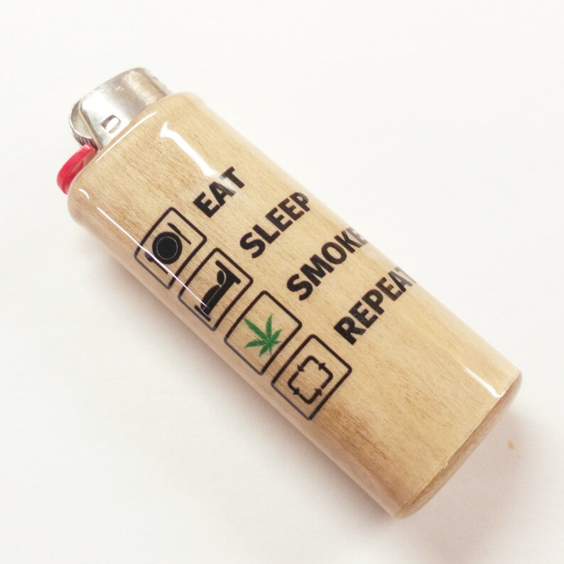 May include: A wooden lighter with a black and green design. The lighter has the text "Eat, Sleep, Smoke, Repeat" printed on it.