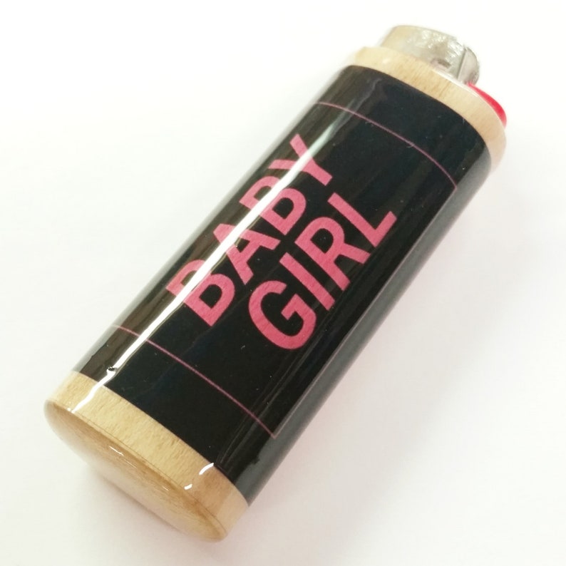 May include: A wooden lighter with a black label that says "BABY GIRL" in pink letters.