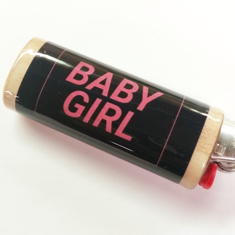 May include: Black lighter with a wood finish and a pink graphic that says "BABY GIRL".