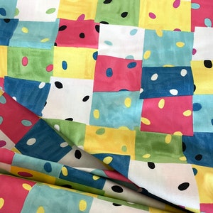 May include: A colorful fabric with a patchwork design featuring squares of yellow, pink, blue, green, and white. Each square is decorated with small dots and ovals in various colors.