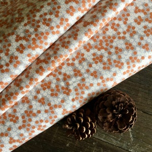 May include: White fabric with a repeating pattern of small orange flowers. The fabric is folded in half and the edges are visible. The fabric is lying on a brown wooden surface.