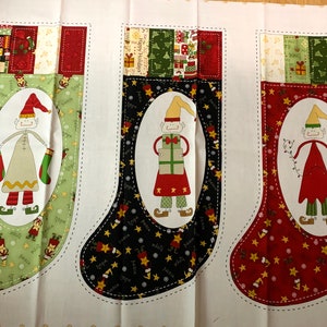 May include: Three Christmas stockings with elf designs. The stockings feature green, black, and red backgrounds with star and elf patterns. Each stocking has an oval-shaped elf illustration in the center, with a decorative top.