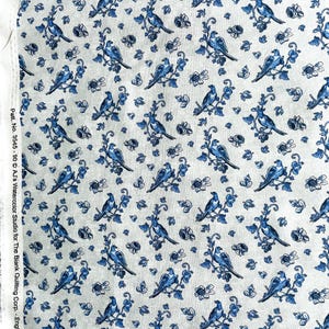 May include: A white fabric with a repeating pattern of blue birds perched on branches with small white flowers. The fabric has a subtle linen texture.