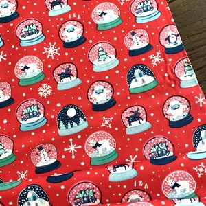 May include: Red fabric with a repeating pattern of snow globes. Each snow globe contains a different winter scene, including a snowman, a penguin, a reindeer, a house, a Christmas tree, and a polar bear. The fabric is perfect for crafting projects like pillows, blankets, and bags.