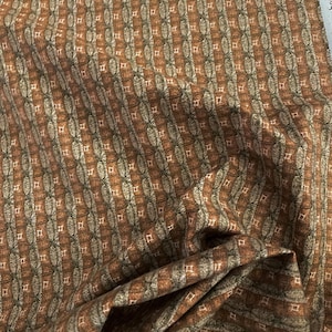 May include: Brown fabric with a repeating pattern of small squares and ovals. The fabric has a subtle sheen and a slightly textured surface.