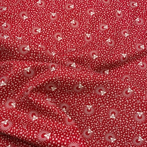 May include: Red fabric with a white geometric pattern. The pattern is made up of small circles and stars.