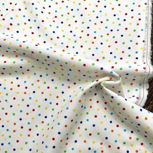 May include: White fabric with a repeating pattern of colorful polka dots in red, orange, yellow, green, and blue. The fabric is folded, showing the texture and the raw edge of the material.