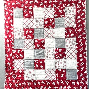 May include: A red and white patchwork quilt with a white border. The quilt is made of squares with different patterns, including snowflakes, plaid, and bears.