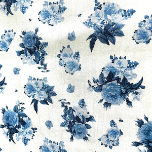 May include: White fabric with a repeating pattern of blue roses and foliage. The floral design features various sizes of rose bouquets and scattered leaves, creating a classic, vintage aesthetic. The fabric has a slightly textured appearance.