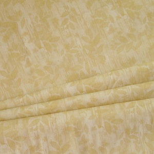 May include: A close-up of a pale yellow fabric with a subtle white floral pattern. The fabric is folded in thirds, showing the texture and design.