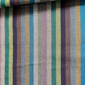 May include: Close-up of a fabric with vertical stripes in various colors. The stripes include shades of teal, green, purple, brown, gray, and gold. The fabric appears to be folded over in the upper right corner.