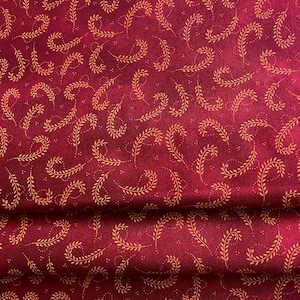 May include: Red fabric with a repeating pattern of small, gold, stylized leaves. The fabric is folded in thirds.