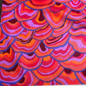 May include: A fabric with a repeating pattern of colorful, layered, concentric circles resembling agate or a cross-section of a tree trunk. The colors are shades of red, orange, pink, purple, and blue.