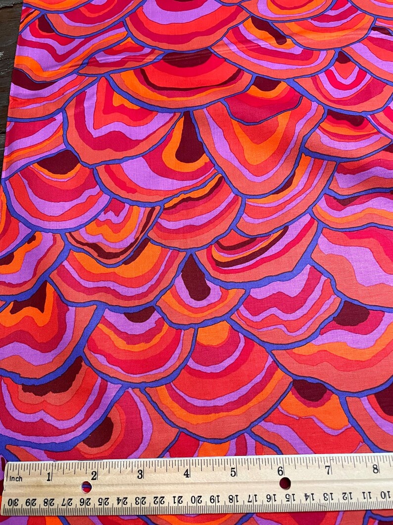 May include: A fabric with a repeating pattern of colorful, layered, concentric circles resembling agate or a cross-section of a tree trunk. The colors are shades of red, orange, pink, purple, and blue.