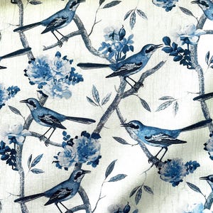 May include: A white fabric with a blue floral and bird pattern. The birds are blue and white and are perched on branches. The flowers are blue and white and are in clusters.
