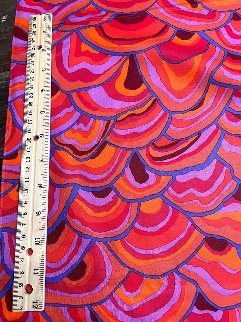 May include: A fabric with a repeating pattern of overlapping, concentric circles in shades of orange, red, and purple. The circles are outlined in blue.
