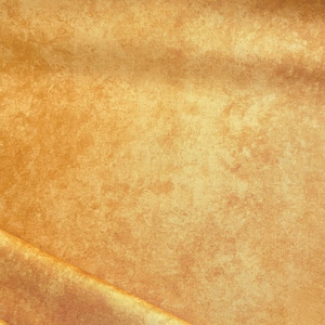 May include: A close-up shot of a golden-yellow fabric with a textured, mottled appearance. The material has a subtle sheen and a pattern reminiscent of aged or distressed surfaces. The fabric is folded, creating shadows and highlighting the texture.