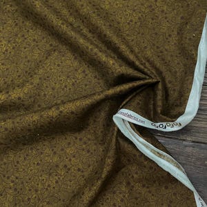 May include: A close-up of a brown fabric with a dark brown floral pattern. The fabric has a subtle sheen and a soft texture. The fabric is folded in half and the edge is visible. The fabric is labeled "Glassfabrics.net".