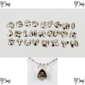 Puede incluir: Encantos de letras de alfabeto de plata con un solo strass en cada letra. Los encantos se muestran sobre un fondo blanco. También se muestra un collar de cadena de plata con un solo encanto de letra.