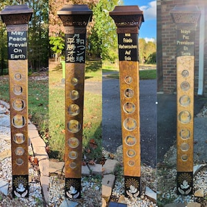 May include: A tall, bronze-colored outdoor pillar with a decorative top and base. The pillar has several circular cutouts and the text "May Peace Prevail On Earth" in white. A hand and dove design is at the base.