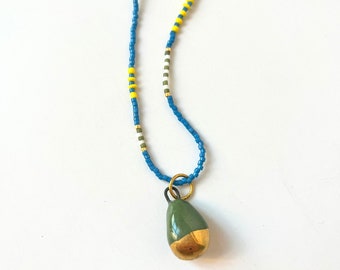 Blue miyuki bead necklace with green, white and yellow beads in striped patterns, with a drop-shaped pendant with gold lustre detail