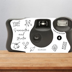 May include: A white disposable camera with black accents and a flash. The camera has various wedding-themed illustrations and the text "Yay! Samantha and Hunter 22.08.2029" printed on it.