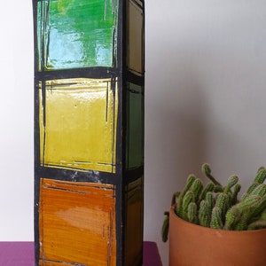 Op de afbeelding: Een hoge, keramische vaas met een geometrisch ontwerp. De vaas is zwart met vierkanten in groen, geel en oranje.