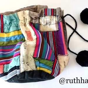 Könnte beinhalten: Eine Patchwork-Kordeltasche aus buntem gestreiftem Stoff mit einer schwarzen Kordel und zwei schwarzen Bommeln. Die Tasche hat ein Etikett mit der Aufschrift "C.M. Linen Fabrics Ltd."