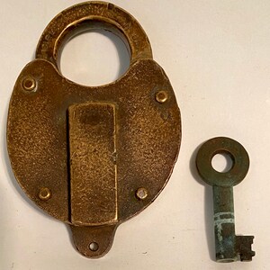 May include: A vintage brass padlock with a key. The padlock is round in shape and has a keyhole on the side. The key is made of brass and has a simple design.