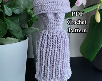 May include: A lavender crochet dress displayed on a small stand. The dress has a detailed bodice and a flared skirt. The image includes the text "PDF Crochet Pattern". The background features plants and flowers.