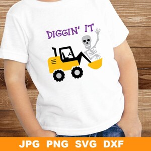 Peut inclure: Un t-shirt blanc avec le texte "Diggin' It" en lettres violettes. Un squelette de dessin animé conduit un véhicule de chantier jaune avec une pelle.