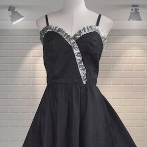 May include: A black dress with a sweetheart neckline and a full skirt. The bodice is accented with silver trim along the neckline and a diagonal detail. The dress is displayed on a mannequin.