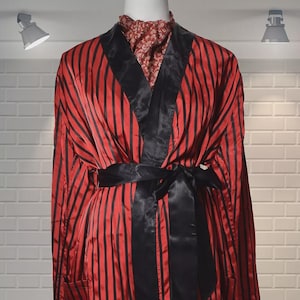 May include: A red and black striped robe with a black satin trim and a matching belt. The robe has long sleeves and pockets. The mannequin is wearing a patterned top underneath the robe.
